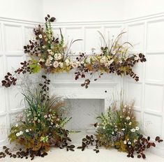 an arrangement of flowers and plants in front of a fireplace