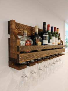 a wooden wine rack filled with bottles and glasses on top of a white wall next to a window