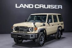 a beige land cruiser parked in front of a black wall