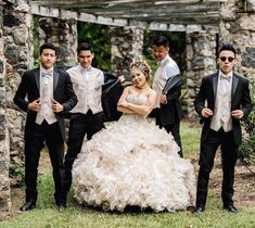 a group of people standing next to each other in front of a stone structure wearing tuxedos