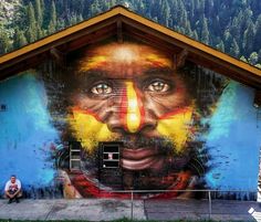 a man sitting in front of a building with a mural on it's side