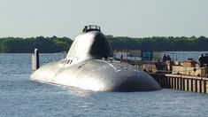 a submarine sitting in the water near a dock with people standing on it's side