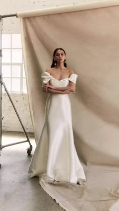 a woman standing in front of a white backdrop with her arms crossed and looking off to the side