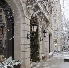 snow falling on the ground and street lights in front of a building with arched doorways