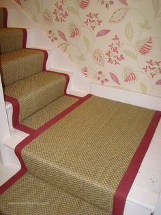 a carpeted stair case next to a wall with flowers on it and a red strip at the bottom