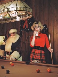 two people dressed up as santa claus and a woman in a red sweater playing pool