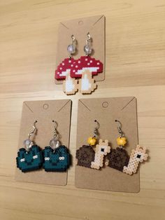 four pieces of pixelated earrings are displayed on a wooden table with tags attached to them