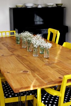 a wooden table topped with yellow chairs and vases filled with baby's breath flowers