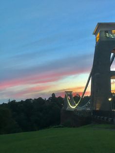 the sun is setting behind a bridge with lights on