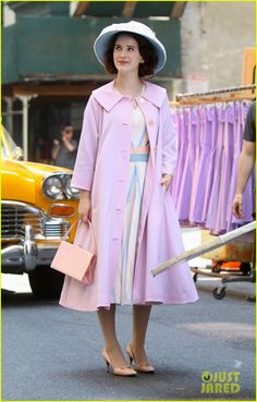 a woman in a pink coat and hat is standing on the street with her handbag