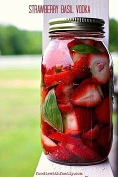 a jar filled with sliced strawberries on top of a wooden table next to grass