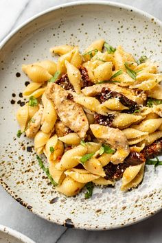 a white bowl filled with pasta and meat on top of a marble countertop next to utensils