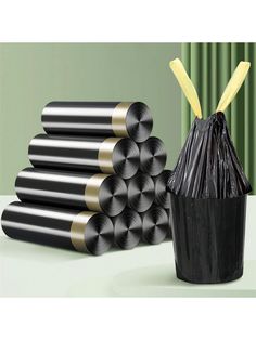 several rolls of black and gold colored paper next to a trash can with two yellow straws in it