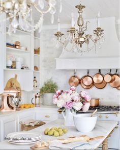 a chandelier hanging from the ceiling in a kitchen with white cabinets and marble counter tops