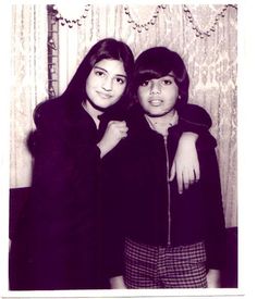 two women standing next to each other in front of a wall with curtains on it