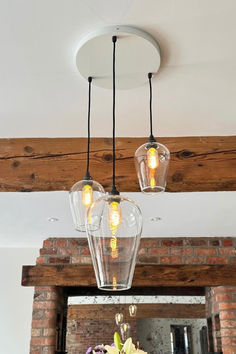 three lights hanging from the ceiling above a dining room table with flowers in vases