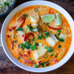 a white bowl filled with soup next to a plate of rice and lime wedges