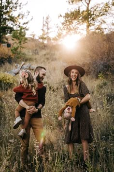 three people are standing in the grass with one holding a dog and another carrying a child