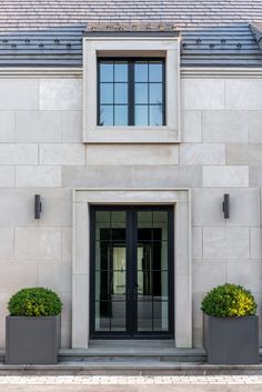 two planters with flowers are in front of a white brick building that has black doors and windows