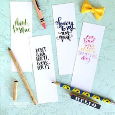 three bookmarks with writing on them next to markers and pencils, one has a yellow bow tie