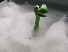 a green toy sitting in foamy water next to a faucet with its mouth open