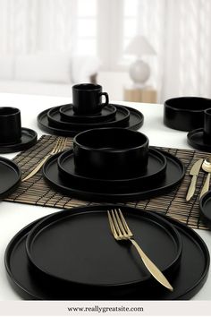 a table set with black plates and goldware