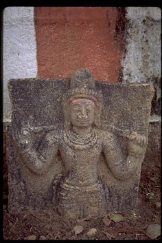 a stone statue sitting on top of a pile of dirt next to a brick wall