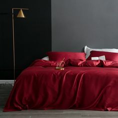 a bed with red sheets and pillows in a room next to a lamp on the floor