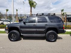 a black suv parked in front of a fenced parking lot next to palm trees