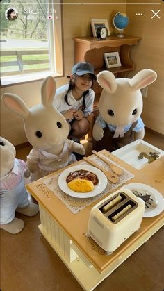 two stuffed animals sitting at a table with food on it and a woman standing next to them