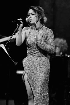 a woman in a long dress singing into a microphone with her hands on her hips