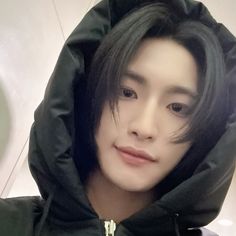 a man with black hair wearing a hoodie and looking at the camera while standing in front of a mirror