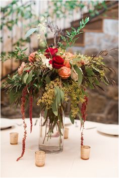 a vase filled with flowers and greenery sitting on top of a white table cloth