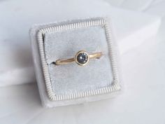 a gold ring with a black diamond sits in a velvet box on a white surface