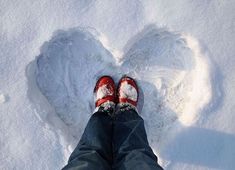 someone wearing red shoes standing in the snow with their feet up and heart - shaped