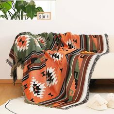 an orange and black blanket sitting on top of a wooden floor next to a white couch