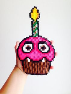 a hand holding a pixelated cupcake with a candle sticking out of it