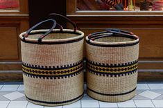 two woven baskets sitting on the ground in front of a store window with their handles down