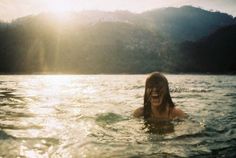 a woman swimming in the water with mountains in the background