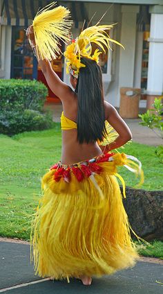 a woman in a yellow hula skirt walking down the street with her hand on her hip