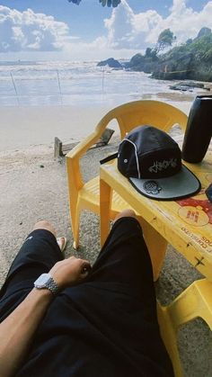 a man laying on top of a yellow bench next to the ocean with a hat on it