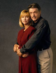 a man and woman standing next to each other in front of a black background with their arms around each other