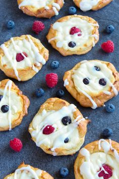 blueberries, raspberries and cream cheesecakes are arranged on a baking sheet