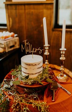 a white cake sitting on top of a wooden table next to two candles and greenery