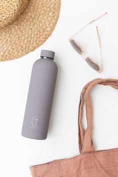 a gray water bottle sitting on top of a bag next to sunglasses and a straw hat