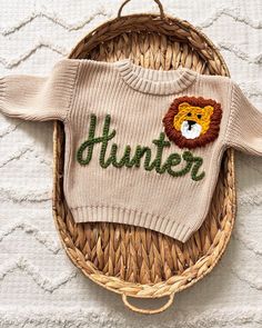 a knitted sweater with the word hunter on it and a lion head is hanging from a wicker basket