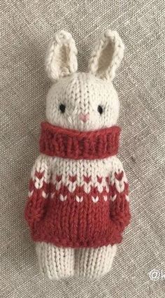 a knitted bunny wearing a red and white sweater on top of a gray surface