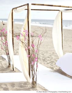 an outdoor ceremony setup on the beach with white linens and flowers in vases