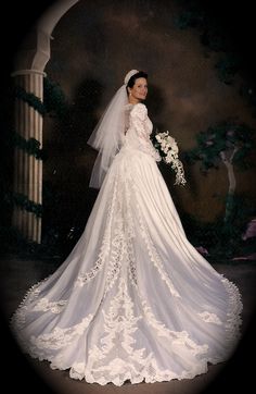 a woman in a white wedding dress posing for a photo with her veil pulled back