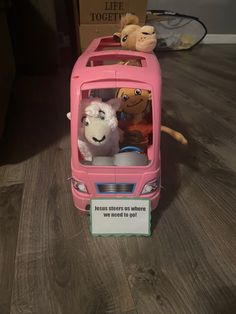 a pink toy bus with stuffed animals in it's back door and sign on the front